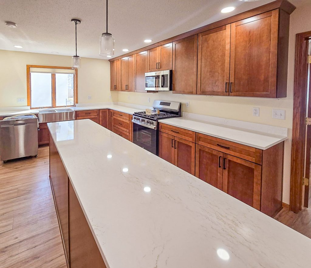 Warm Transitional - Elevated Designs: side partial view of full kitchen with wood cabinets, stainless steel appliances, and wood floors