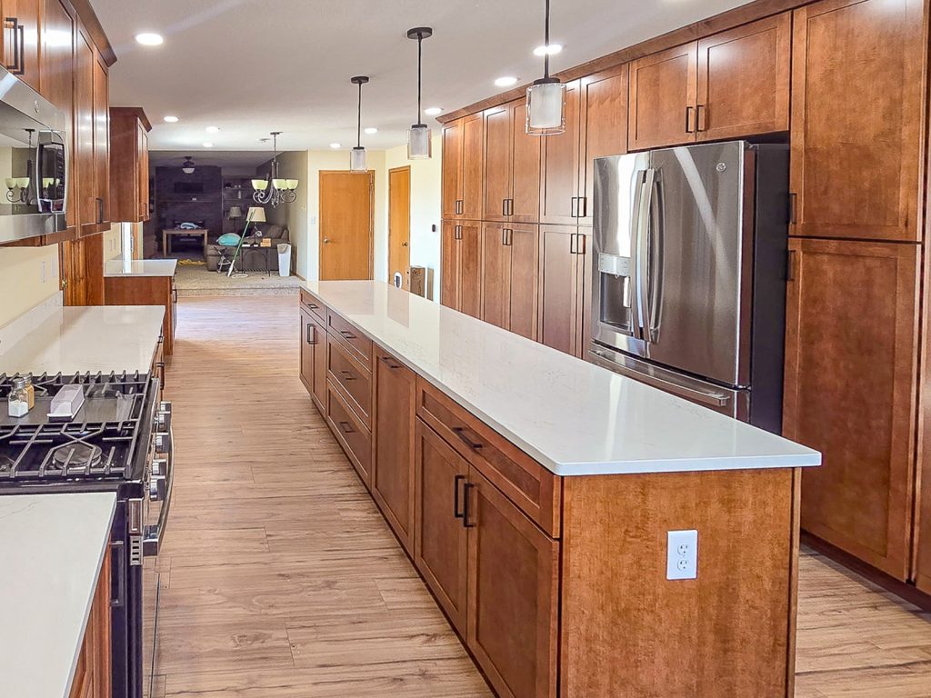Warm Transitional - Elevated Designs: side view of full kitchen with wood cabinets, stainless steel appliances, and wood floors