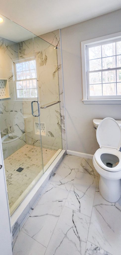 Timeless Master Bath - Elevated Designs: View of toilet and shower with marble floors and glass doors of shower