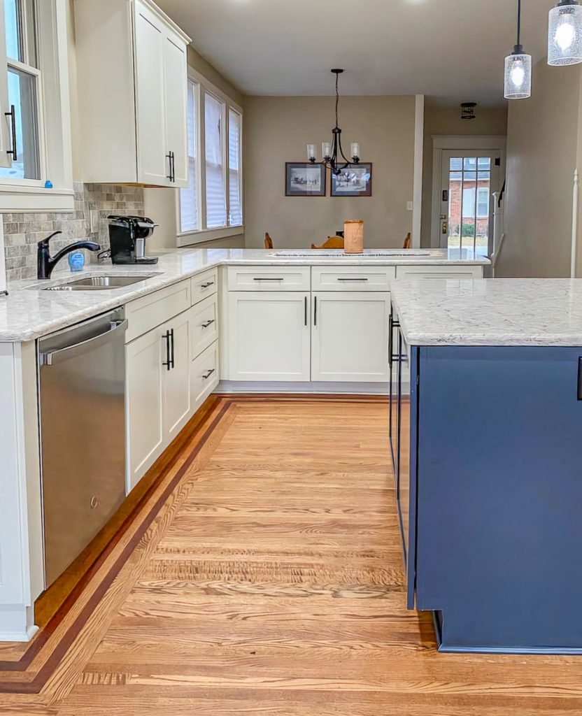 Transitional Charm - Elevated Designs: View of main white cabinet kitchen with marble counters, stainless steel appliances, and wood floors. Partial view of blue island