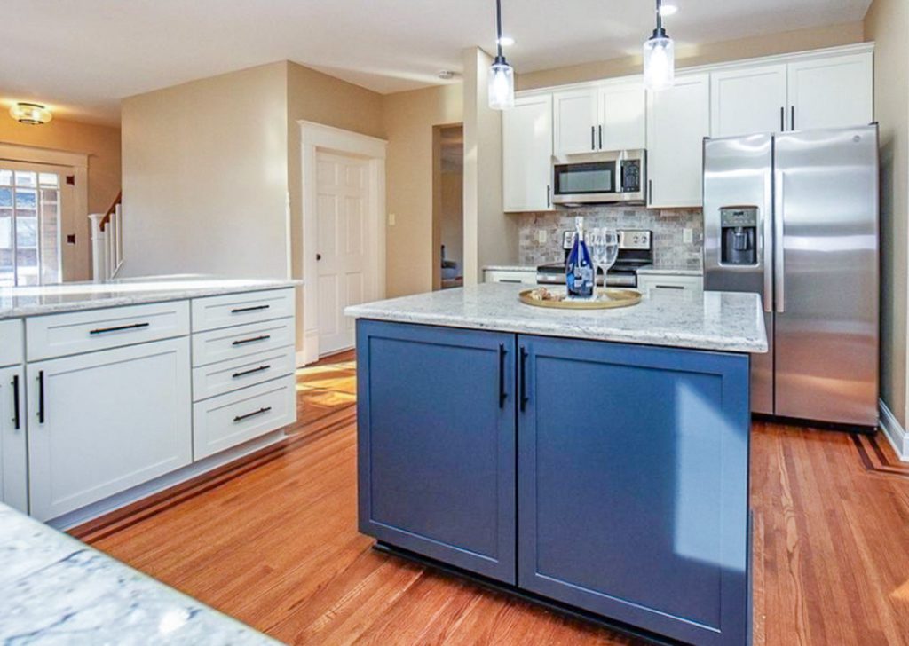 Transitional Charm - Elevated Designs: full View of white cabinet kitchen with marble counters, stainless steel appliances, wood floors. and blue island