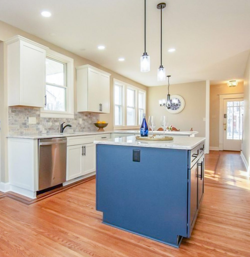 Transitional Charm - Elevated Designs: View of main white cabinet kitchen with marble counters, stainless steel appliances, and wood floors. Partial view of blue island