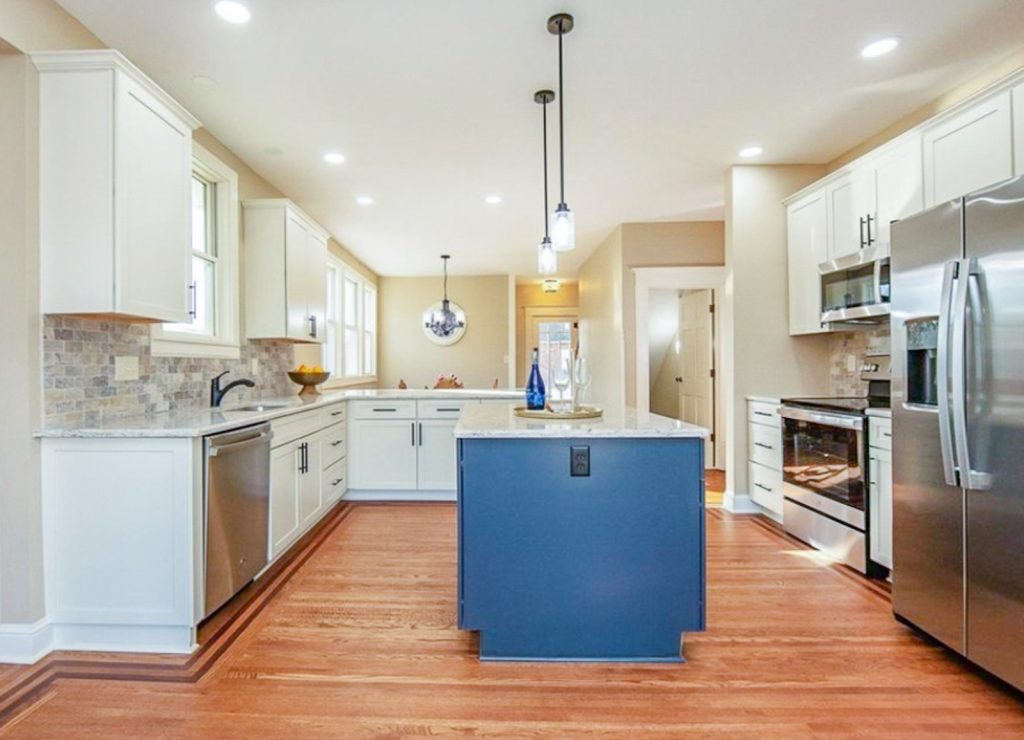 Transitional Charm - Elevated Designs: full View of white cabinet kitchen with marble counters, stainless steel appliances, wood floors. and blue island