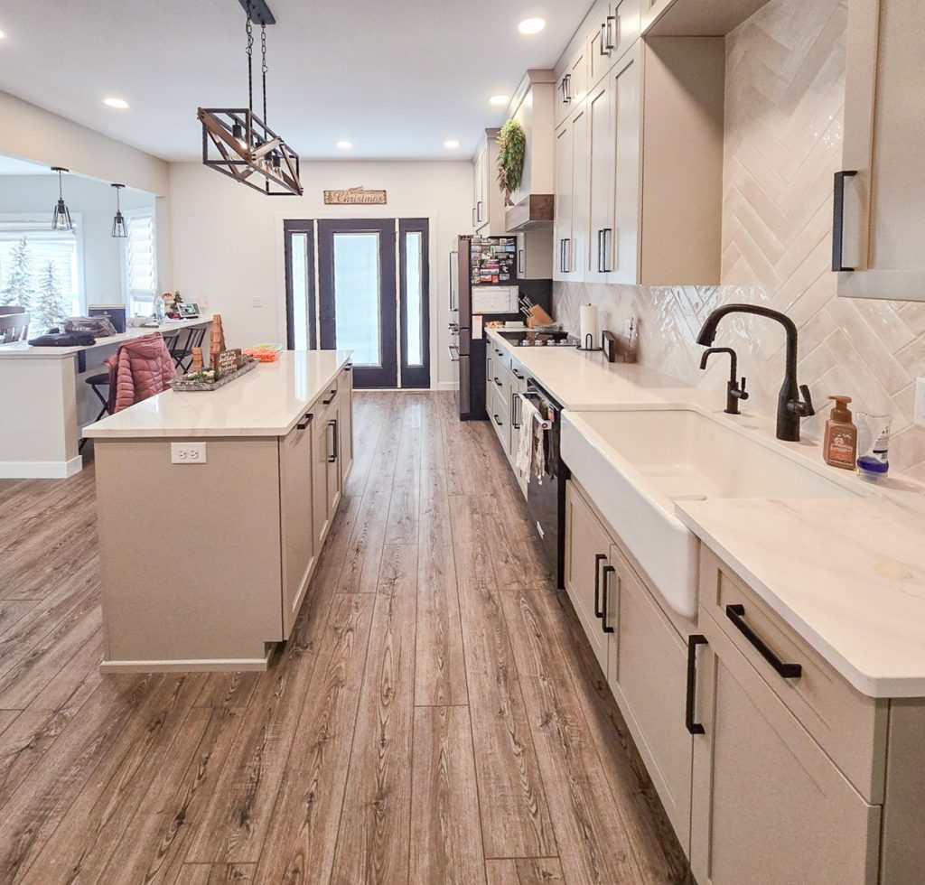 Modern Farmhouse - Elevated Designs: side view of island and sink area of kitchen with white cabinets and wood floors