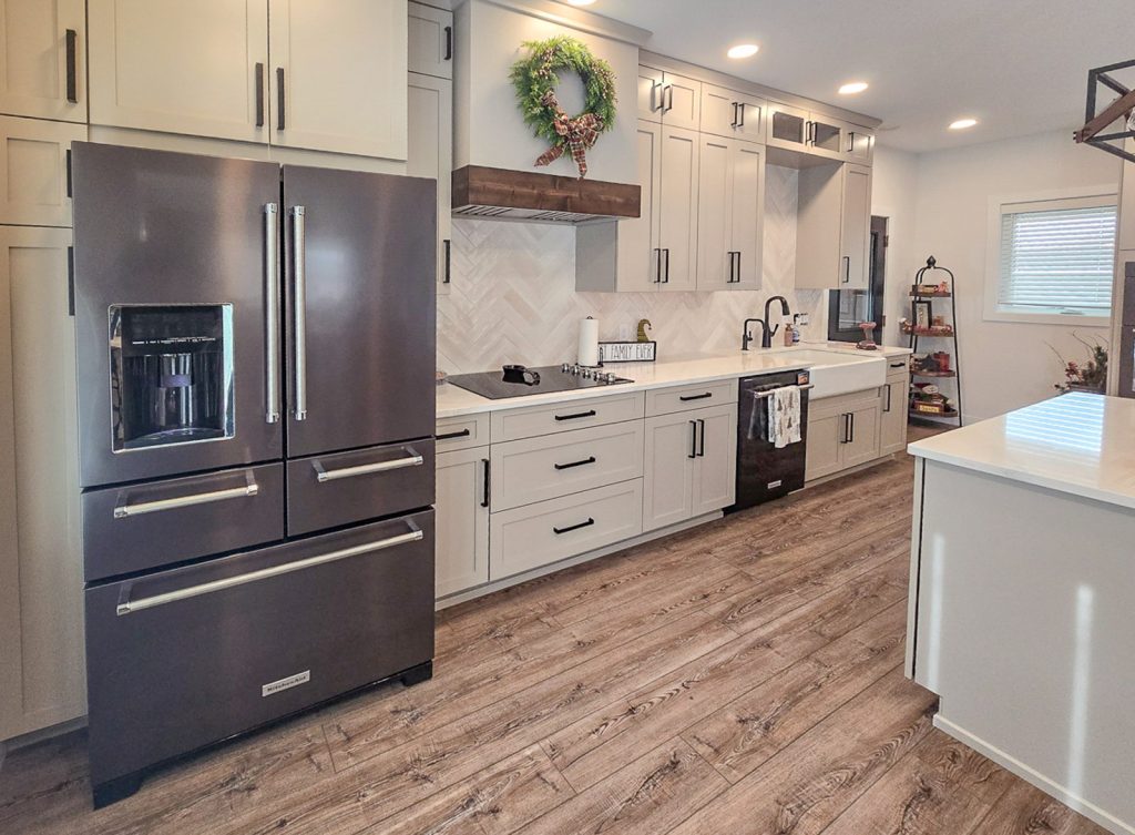 Modern Farmhouse - Elevated Designs: Kitchen with white cabinets, wood floors and stainless steel fridge.